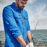 Man in a blue shirt on a boat with fishing gear, looking at something in his hands.